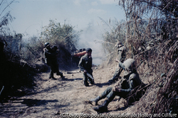 作品画像:南ヴェトナム政府軍によるラオス侵攻作戦。ラオス国境から25キロほど進んだ地点で、装甲車部隊は地雷原に触れて大音響とともに爆発した。その瞬間装甲車からたたき落とされた兵士が、手榴弾銃を右手に膝をつき、さらに左奥では負傷した兵士たちが抱き合っていた。-この連続写真の1枚が『LIFE』1971年3月12日号の表紙となった