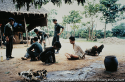 作品画像:カンボジア国境近くの解放区の農村で、政府軍は穴に隠れていた若い農民を捕らえた。「ベトコン」被疑者であるとして、仰向けに倒して顔に布をかぶせ、その上から水を注ぐ拷問を行った。その水をアヒルが飲む