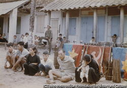 作品画像：捕らえられた解放民族戦線兵士の家族。背後には解放戦線の旗と武器。彼らはこの2時間後に銃殺された