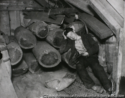 作品画像：（丸太の置かれた小屋で居眠りをする男性）