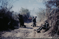 作品画像:南ヴェトナム政府軍によるラオス侵攻作戦。ラオス国境から25キロほど進んだ地点で、装甲車部隊は地雷原に触れて大音響とともに爆発した。その瞬間装甲車からたたき落とされた兵士が、手榴弾銃を右手に膝をつき、さらに左奥では負傷した兵士たちが抱き合っていた。-この連続写真の1枚が『LIFE』1971年3月12日号の表紙となった
