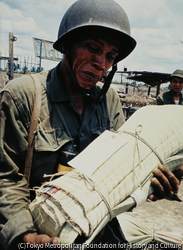 作品画像:解放戦線に襲われ焼けた戦略村で、「写真を写しておくれ」と言い、ムシロに包まれたわが子を抱いて、静かに立ち上がった政府軍の老兵士