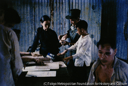 作品画像:逮捕された解放戦線側の一家5人は、指紋を丹念に採られたのち、隠し持っていた武器弾薬とともに公衆の面前に引き出された。その中には0歳の乳児もまじっていたが、射殺されたとみられている