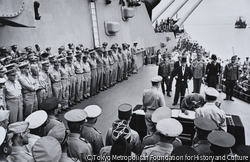 作品画像:米戦艦ミズーリ号上における降伏調印式、1945年9月2日、梅津美治郎参謀総長が降伏文書に署名する。テーブルの前に立つマッカーサー元帥(カメラに背中を向けている)