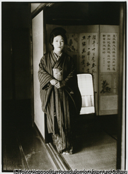 作品画像：立て縞柄模様の着物姿でポーズをつくる芸者。彼女の部屋には大きな鏡台がある
